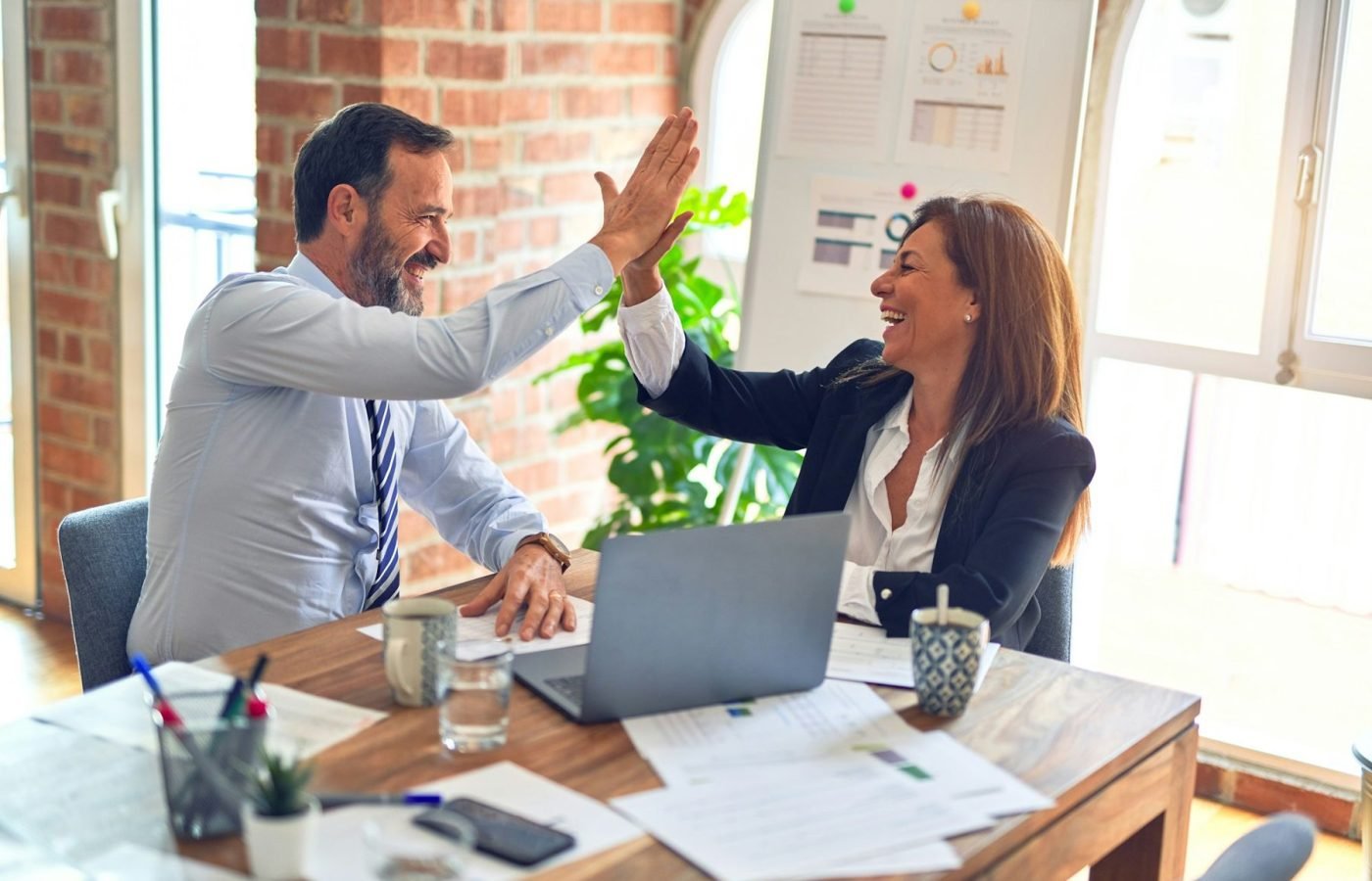 Two colleagues celebrating with a high five at their desk