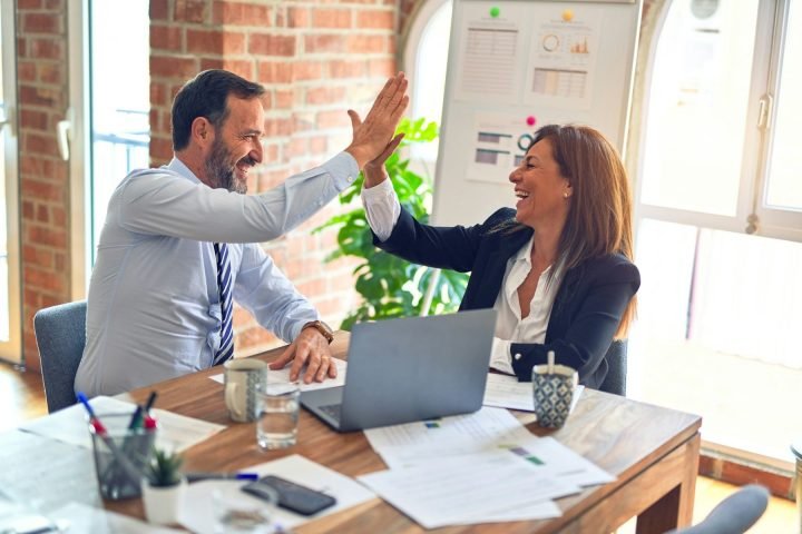 Two colleagues celebrating with a high five at their desk