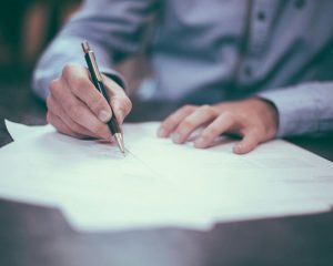 Person signing a printed document with a pen