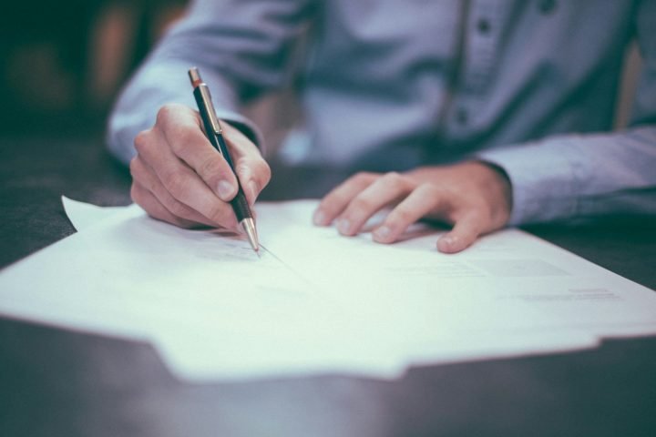 Person signing a printed document with a pen